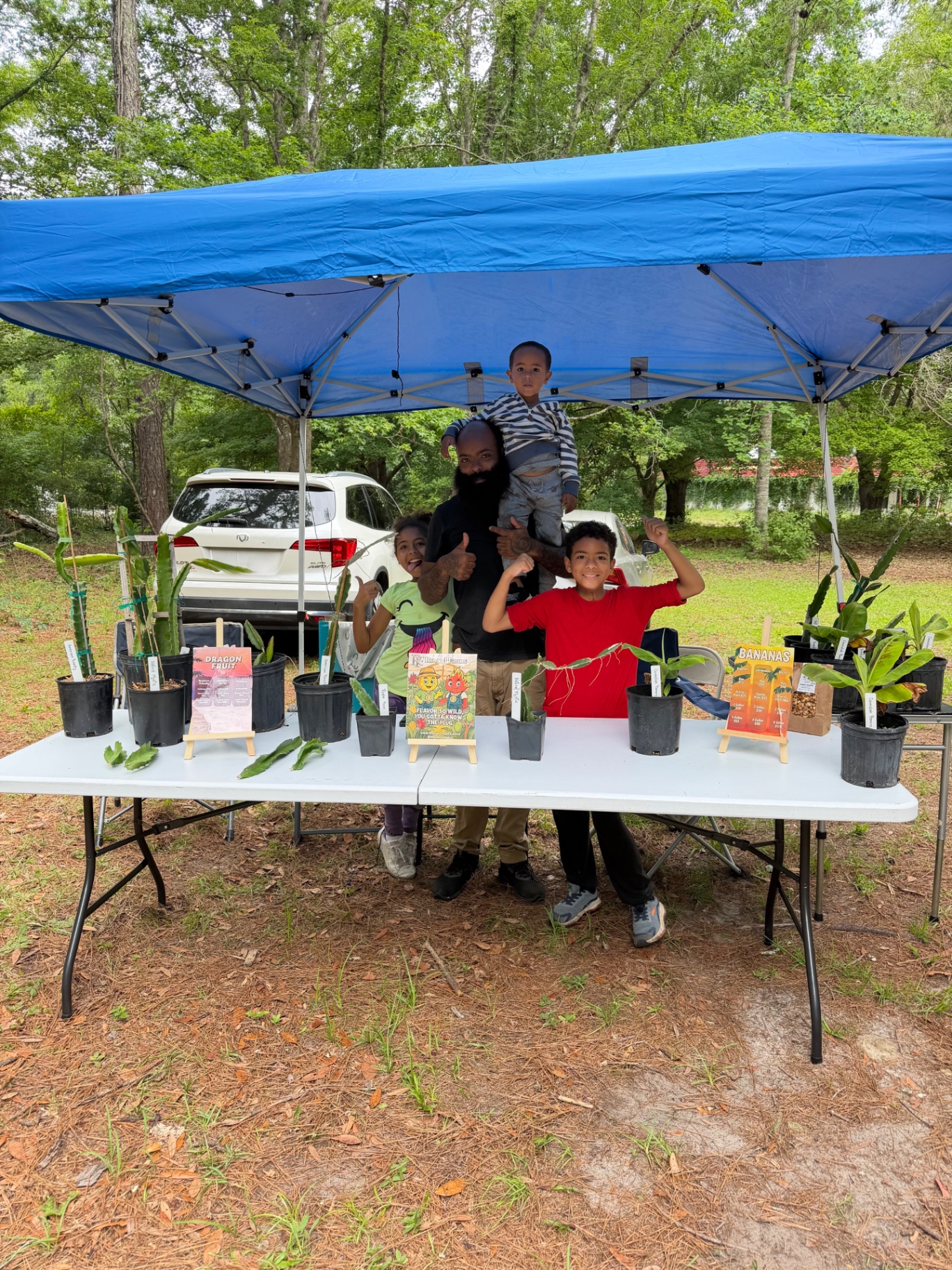 Youth market stand with potted plants and produce under a blue tent